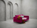 Pink sofa with colorful cushions in a minimalist room with concrete walls and floor.