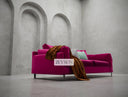Pink sofa with a brown blanket and green pillow in a room with concrete arches.